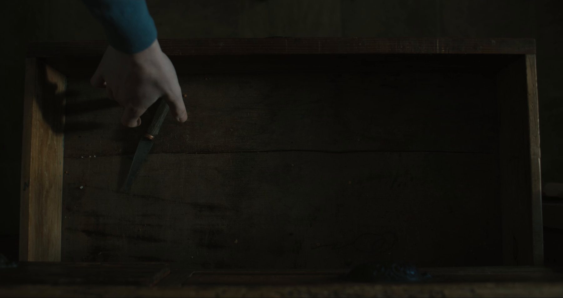 A hand reaching into a drawer for a knife